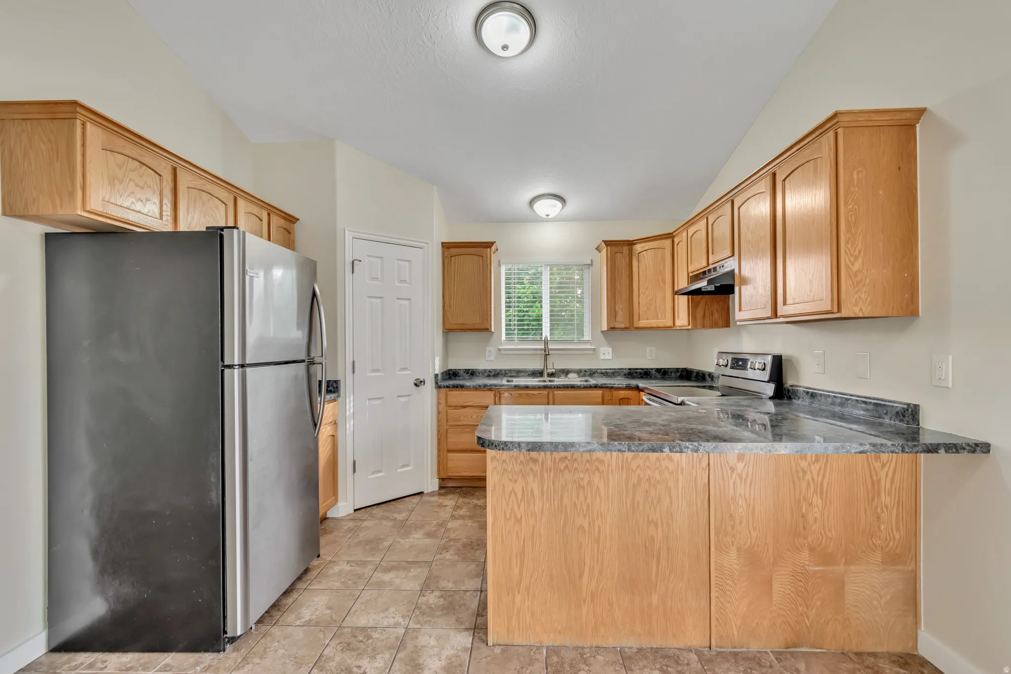 Kitchen featuring stainless steel appliances, a peninsula, dark countertops, and vaulted ceiling