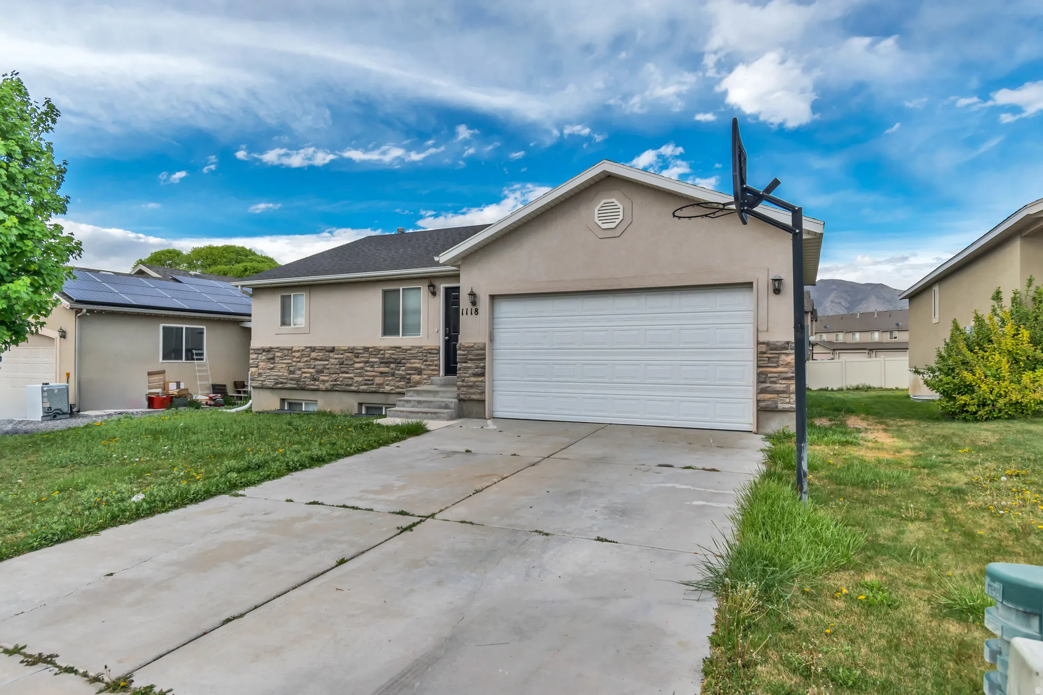 Ranch-style house with stone siding, stucco siding, a garage, a front lawn, and concrete driveway