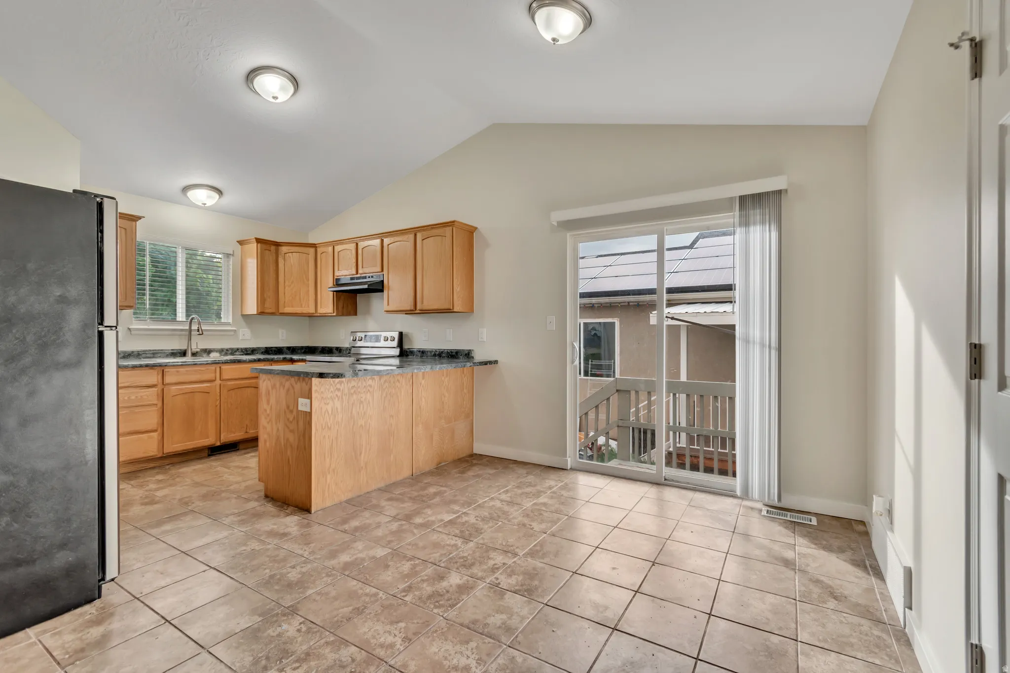 Kitchen with a peninsula, stainless steel appliances, light tile patterned floors, and dark stone counters