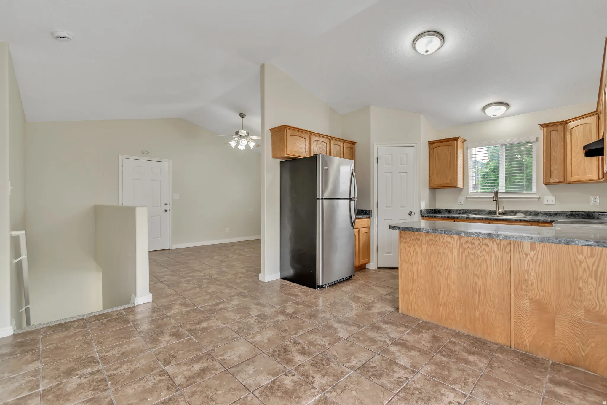 Kitchen featuring freestanding refrigerator, a ceiling fan, vaulted ceiling, and exhaust hood