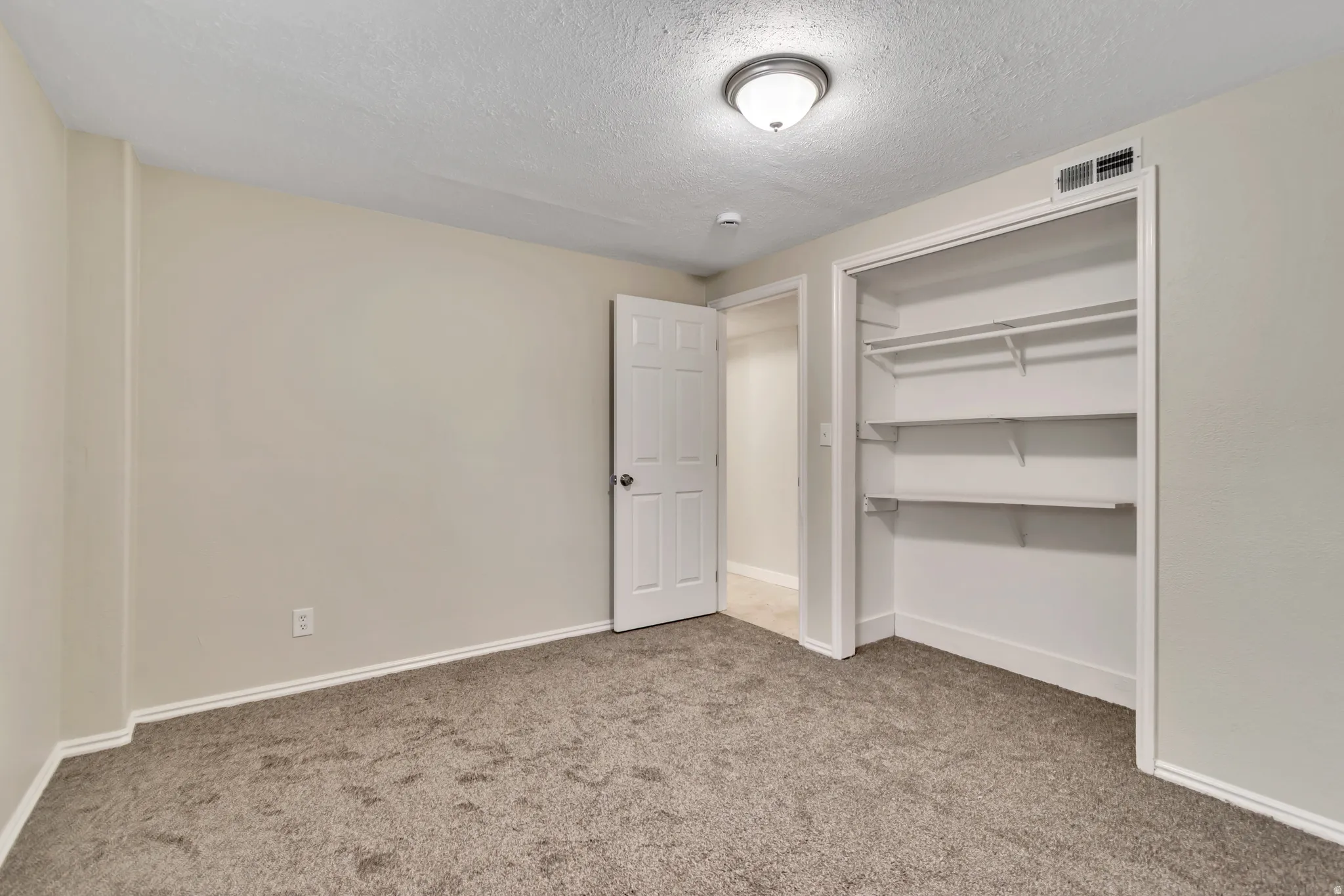 Unfurnished bedroom featuring light carpet, a textured ceiling, and a closet