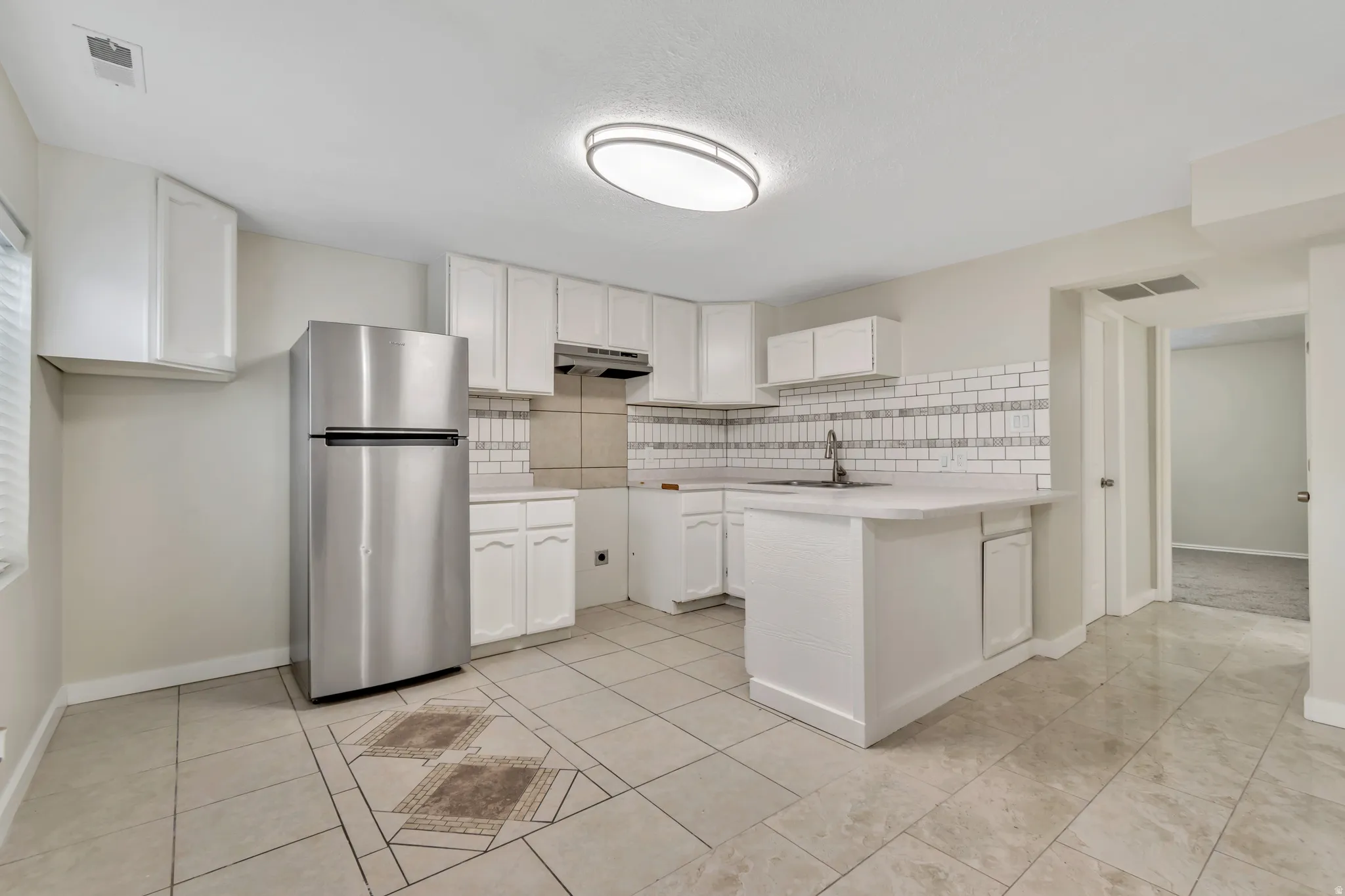 Kitchen featuring freestanding refrigerator, a peninsula, light countertops, white cabinets, and backsplash