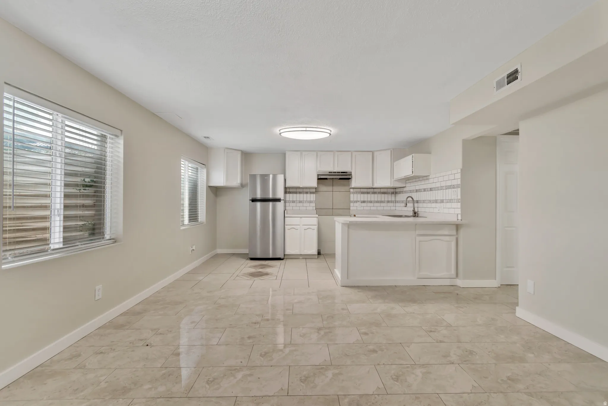 Kitchen with light countertops, freestanding refrigerator, tasteful backsplash, white cabinetry, and a peninsula