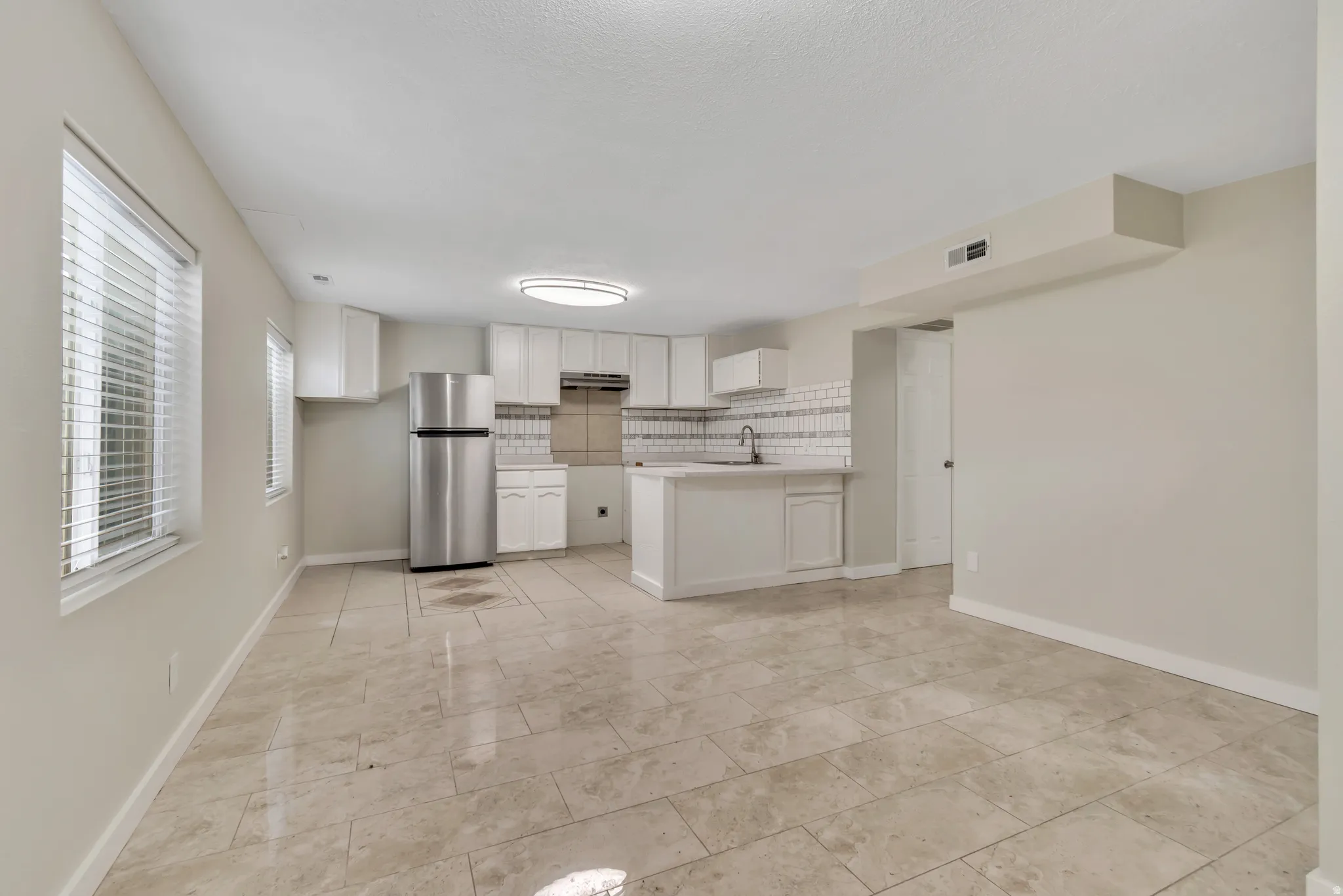 Kitchen featuring freestanding refrigerator, light countertops, white cabinets, decorative backsplash, and a peninsula