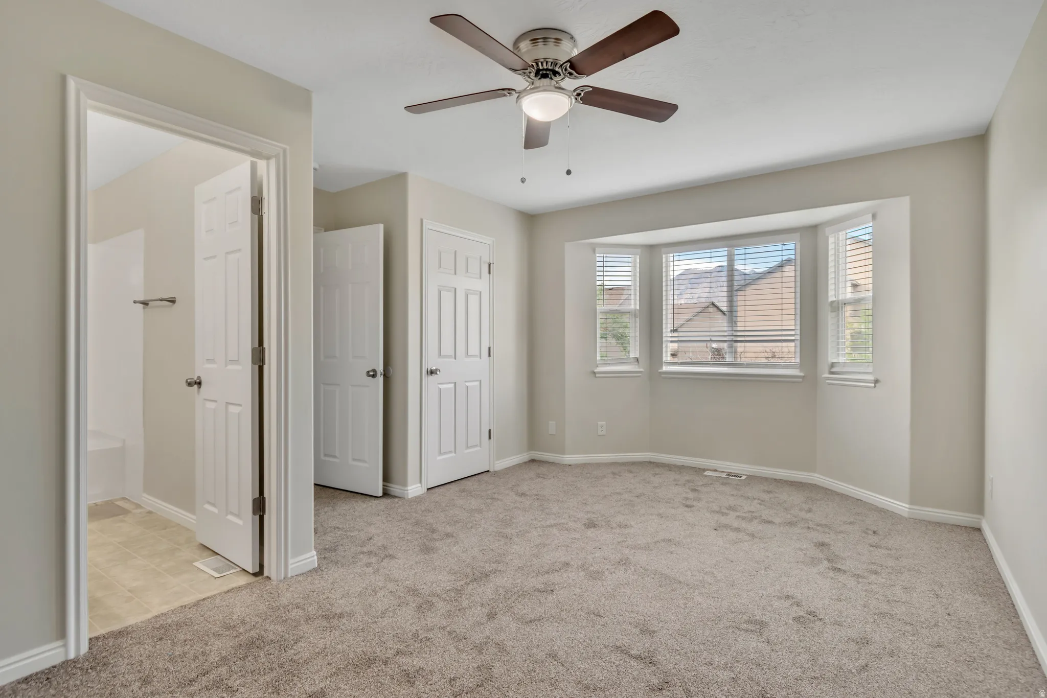 Unfurnished bedroom with light colored carpet, ensuite bath, and ceiling fan
