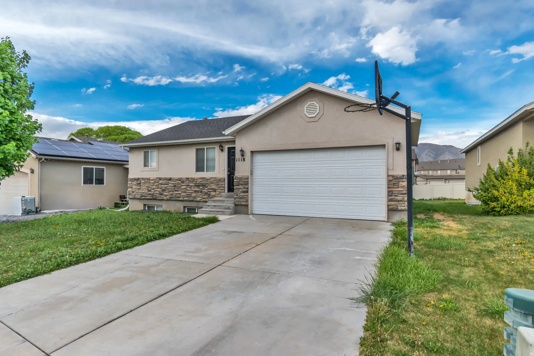 Ranch-style house with stone siding, stucco siding, a garage, and a front lawn
