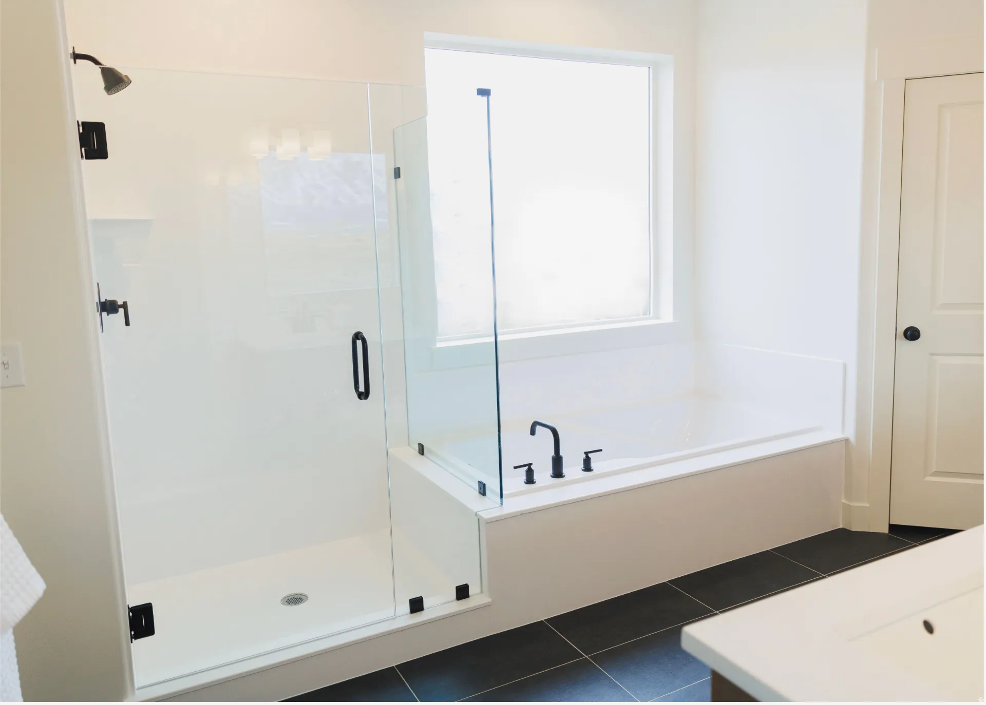 Bathroom featuring a walk-in shower with a glass enclosure, a built-in tub with a window, dark tile flooring, and matte black fixtures