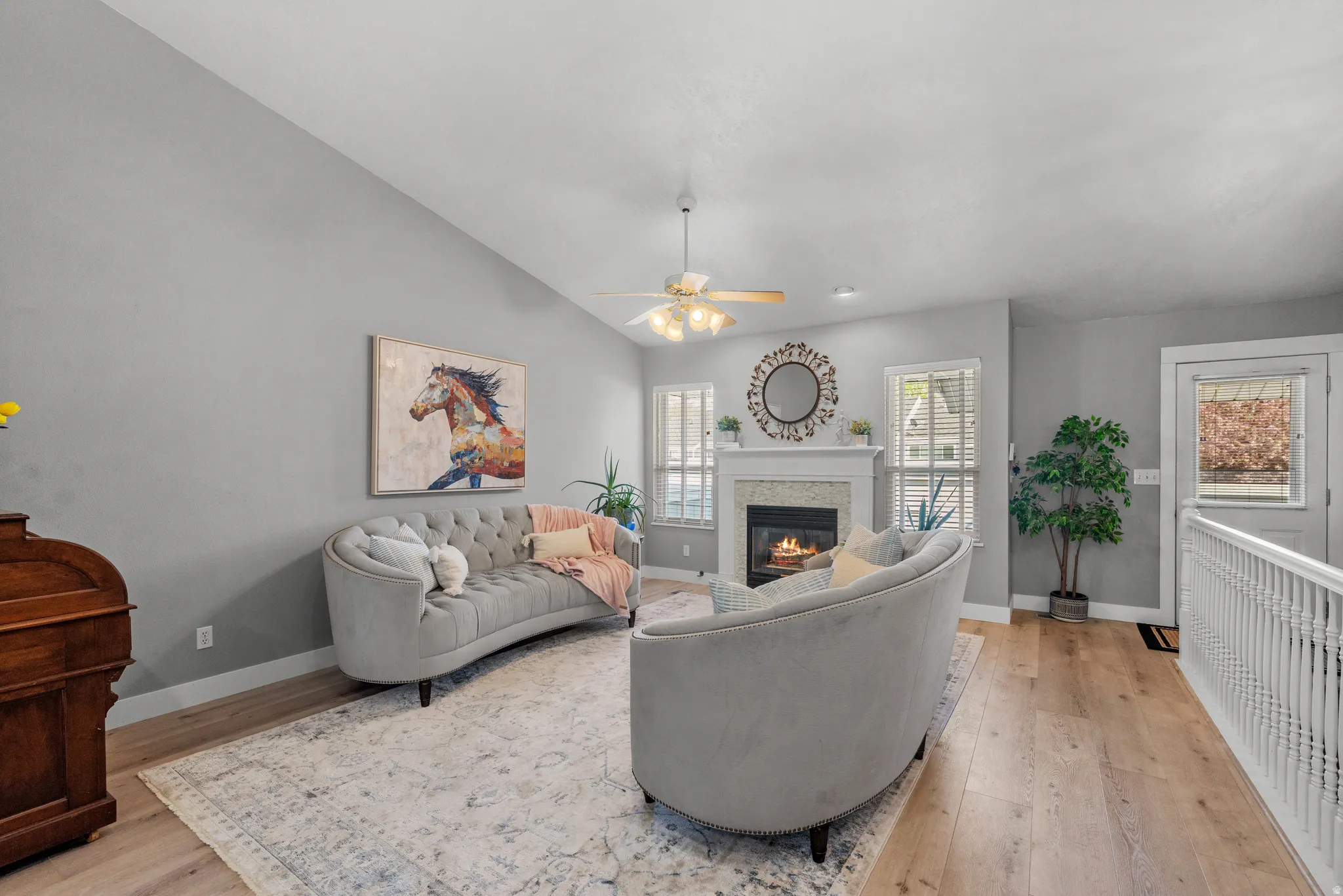 Living area with lots of natural light,  light wood LVP flooring, ceiling fan,  fireplace, and vaulted ceiling