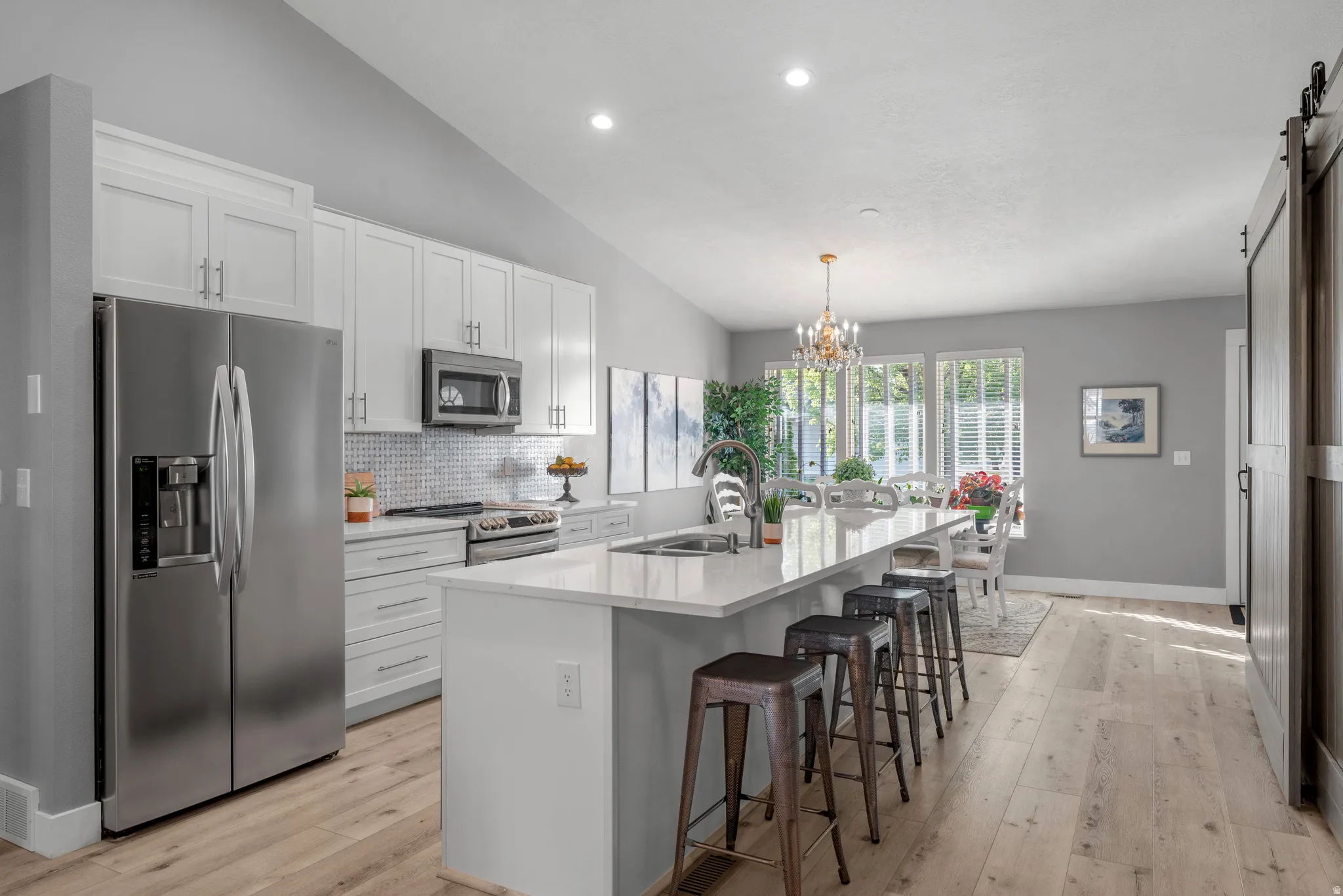 Kitchen with stainless steel appliances, vaulted ceiling, a kitchen bar, an island with sink, and white cabinetry