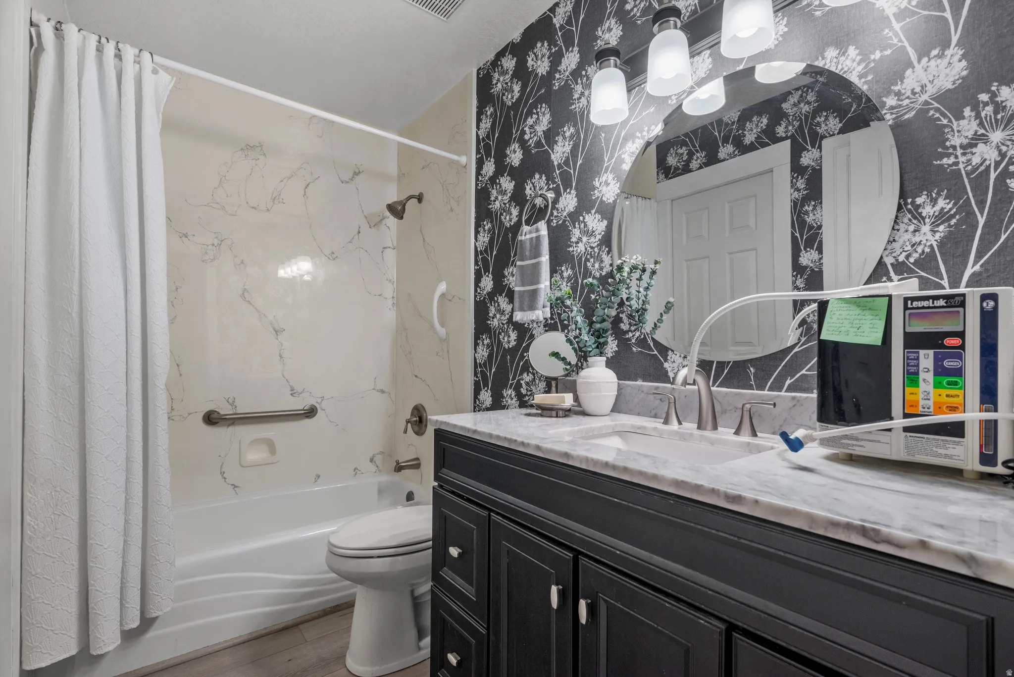 Full bath featuring vanity, shower / tub combo, wallpapered walls, and LVP flooring access from the Primary bedroom and main hallway