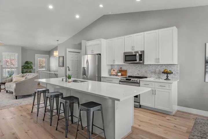 Kitchen featuring open floor plan, stainless steel appliances, a kitchen breakfast bar, white cabinetry, and light wood LVP flooring