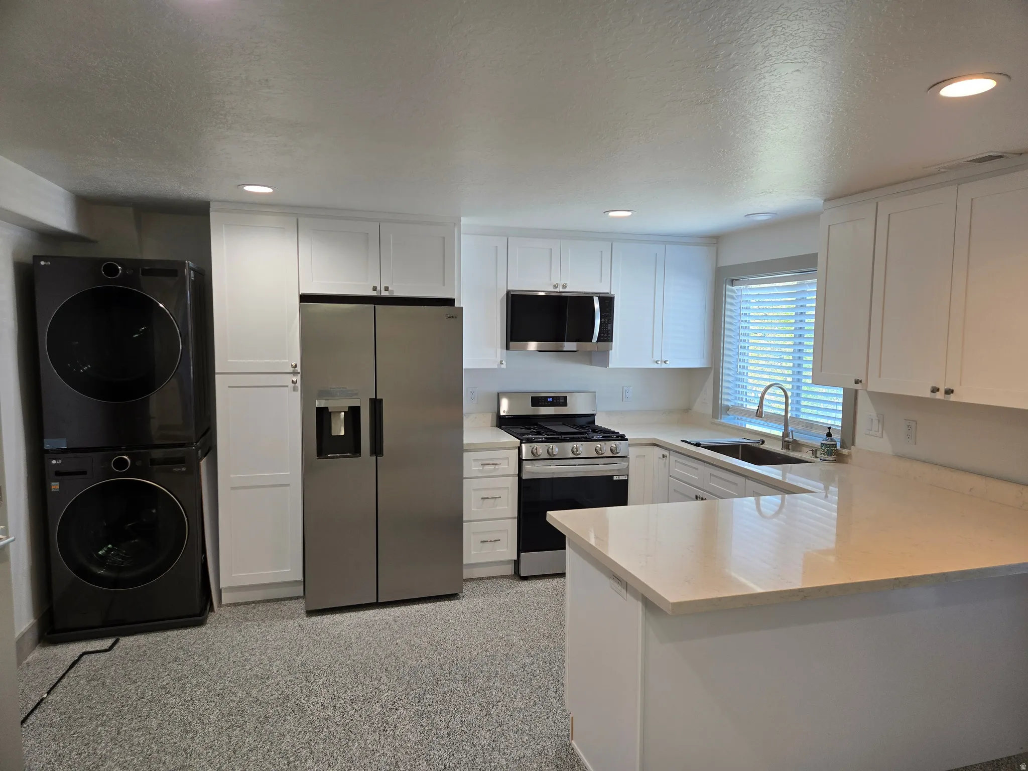 Kitchen featuring stainless steel appliances, a peninsula, white cabinets, a textured ceiling, and recessed lighting