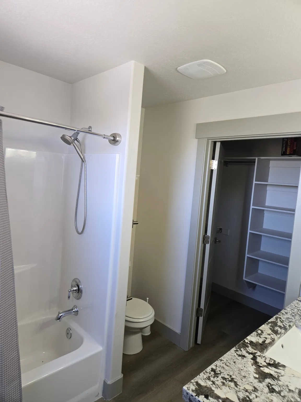 Full bathroom with vanity, dark wood-style floors, shower / bath combo with shower curtain, and a walk in closet