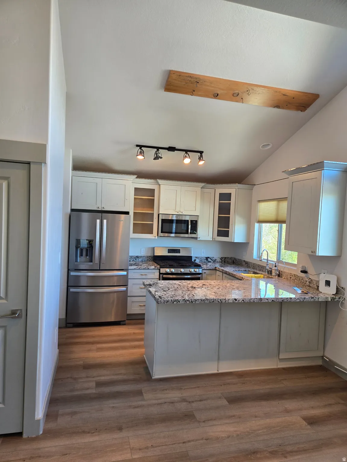 Kitchen with a peninsula, light stone counters, stainless steel appliances, glass insert cabinets, and dark wood-type flooring