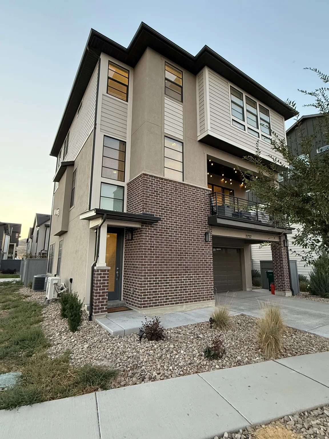 View of front of home with concrete driveway, a balcony, brick siding, an attached garage, and stucco siding
