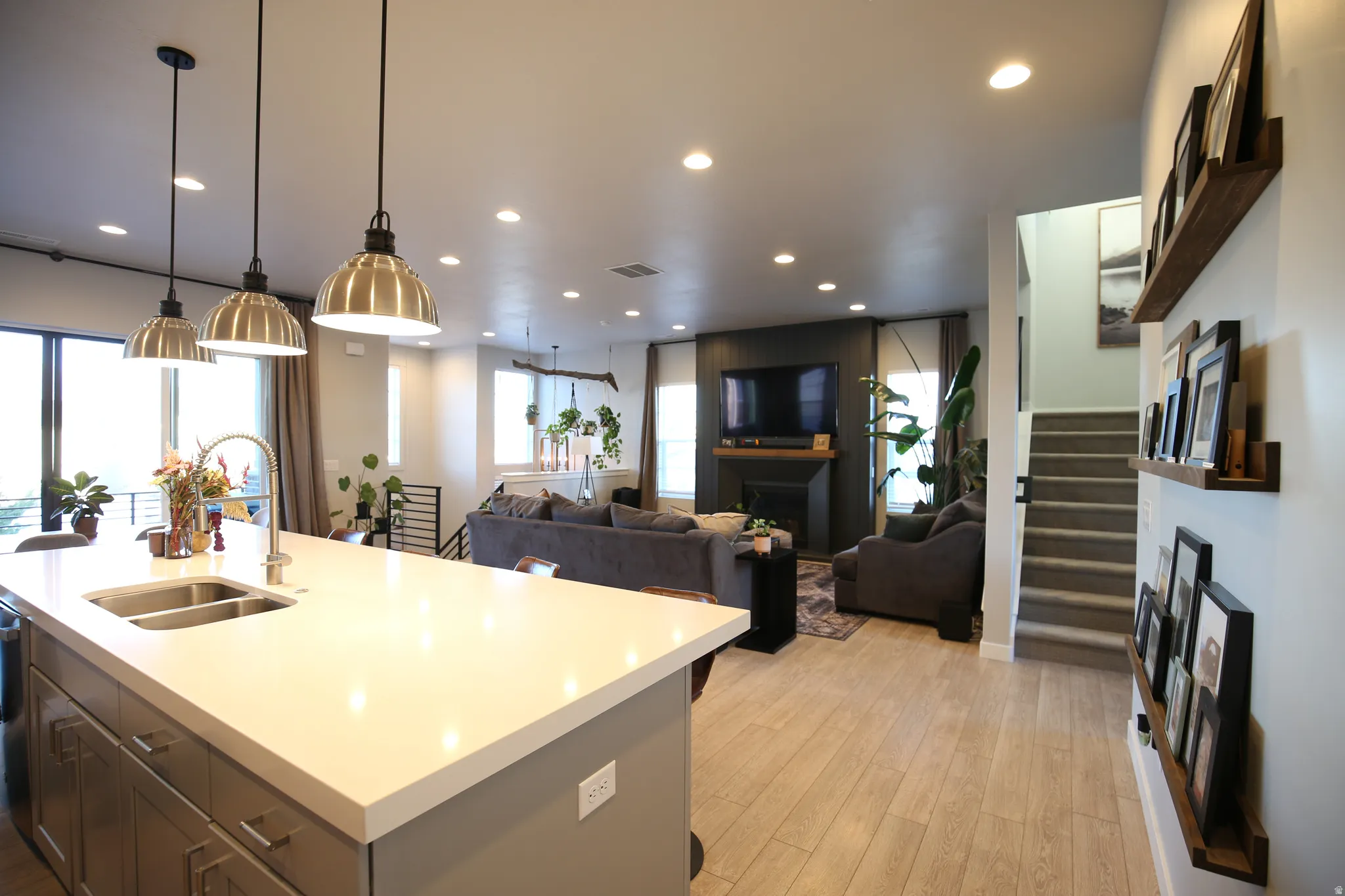 Kitchen featuring open floor plan, light wood-style flooring, an island with sink, light stone counters, and pendant lighting