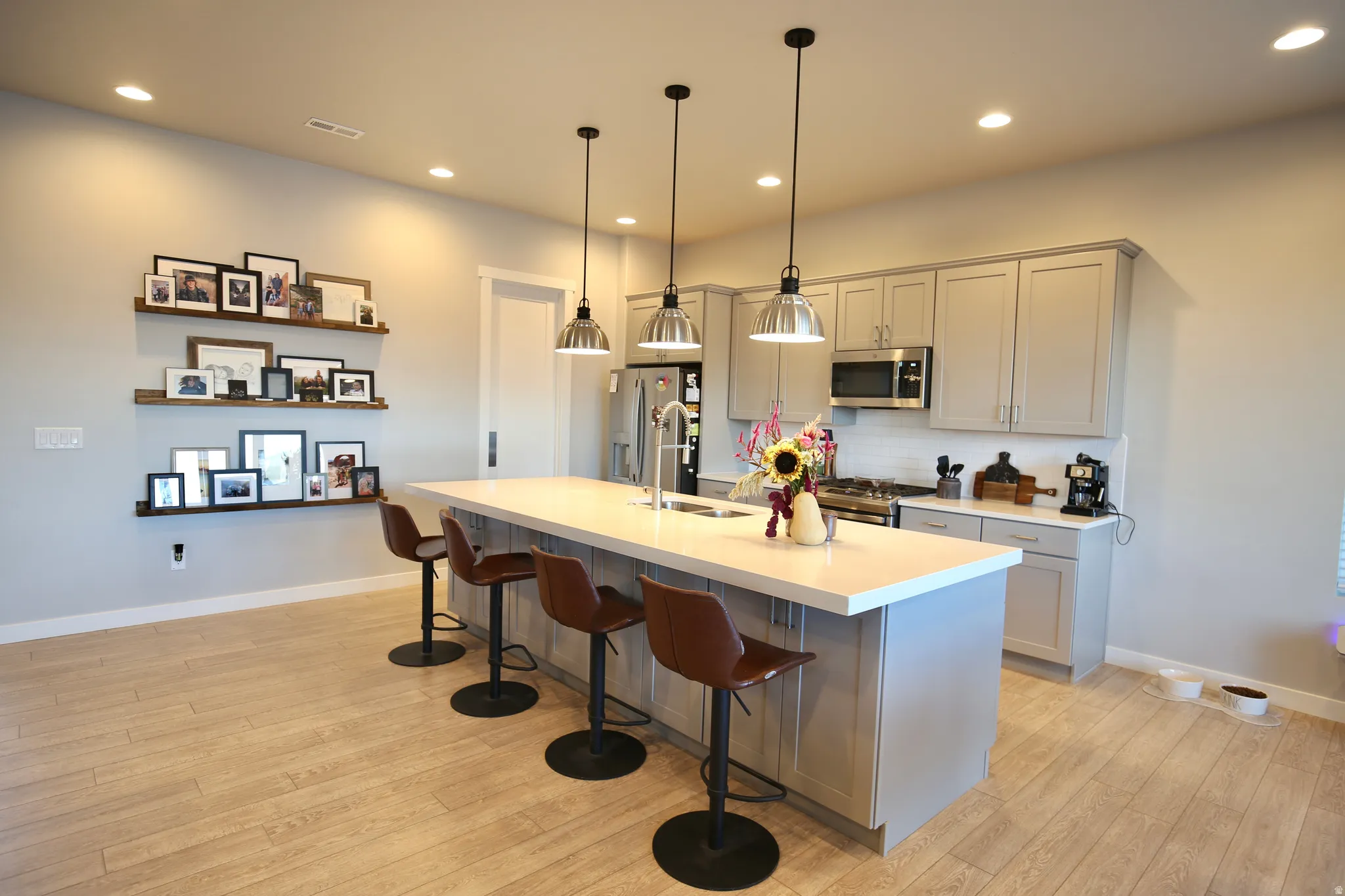 Kitchen with gray cabinets, a breakfast bar area, light wood-type flooring, a kitchen island with sink, and stainless steel appliances