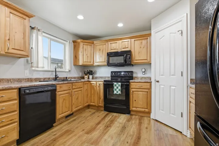 Kitchen featuring black appliances, light wood-style flooring, recessed lighting, light wood finish cabinetry, and light stone counters