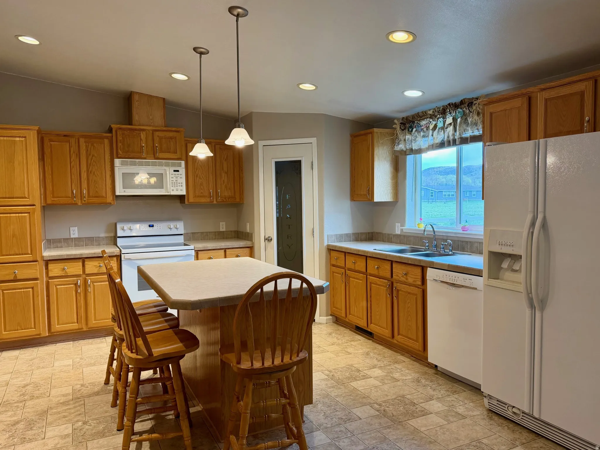 Kitchen featuring white appliances, a center island, light countertops, wood finish cabinets, and pendant lighting