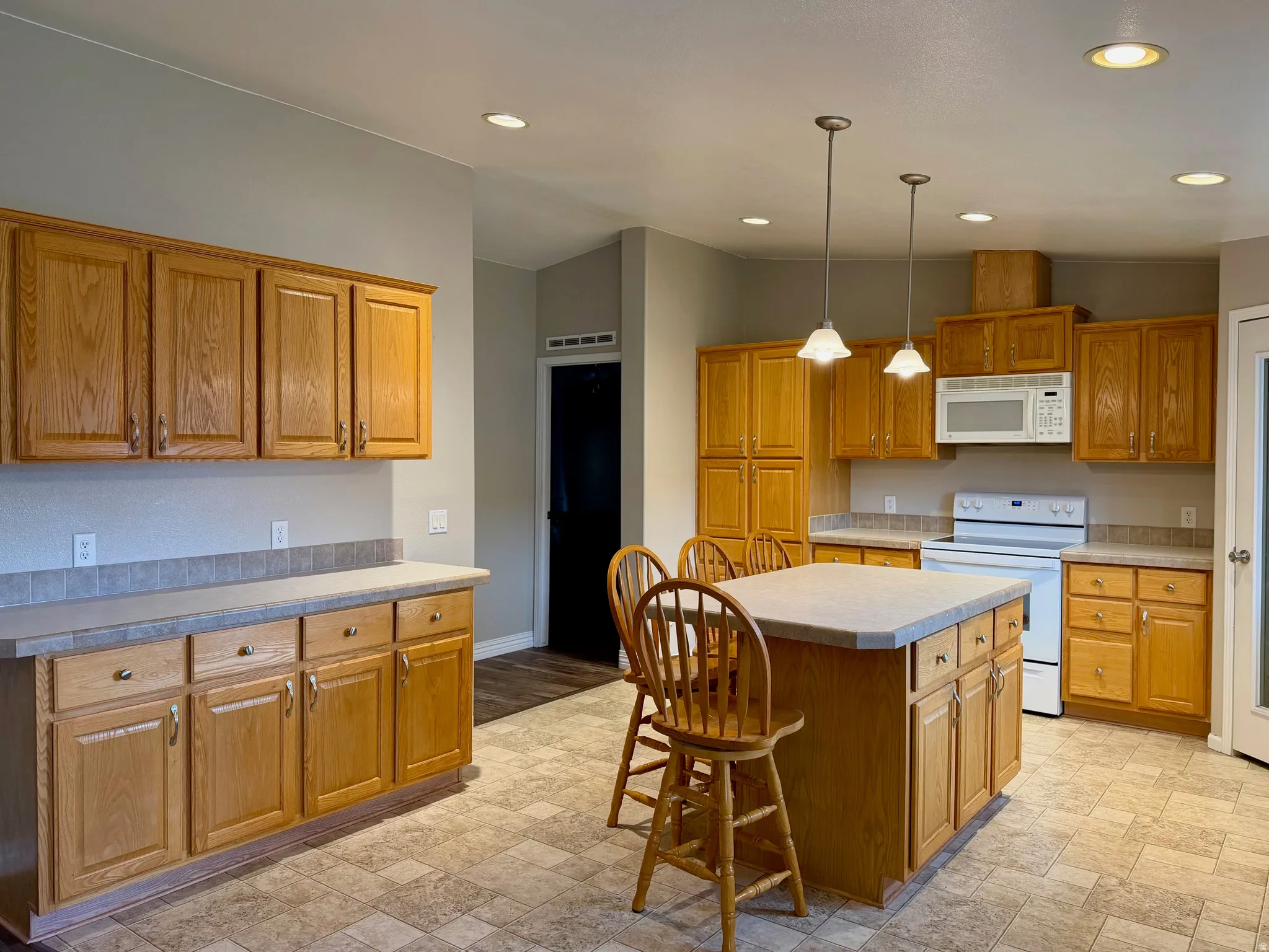 Kitchen featuring a kitchen bar, white appliances, a kitchen island, light countertops, and wood finish cabinets