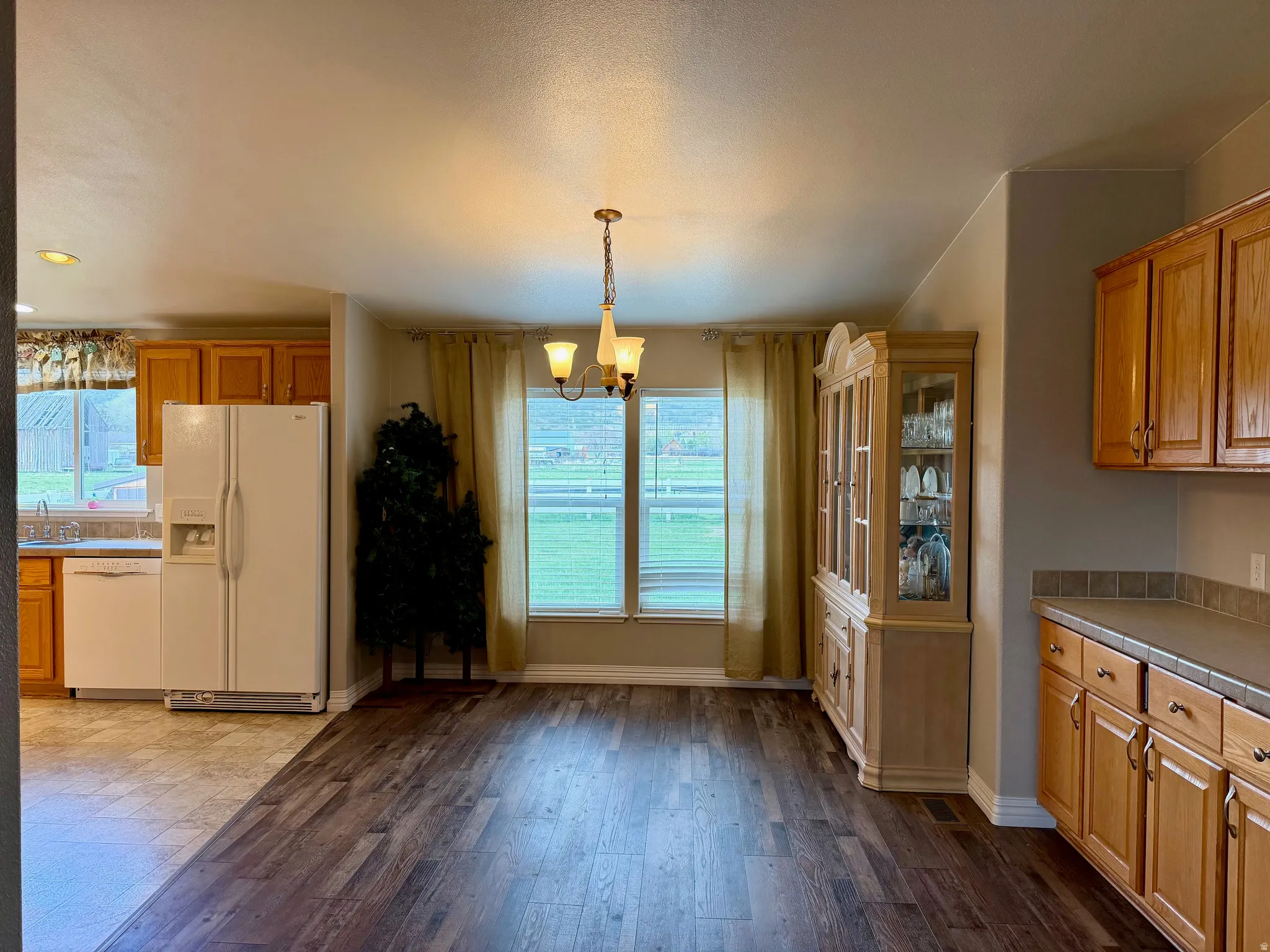 Kitchen featuring white appliances, wood finish cabinets, suspended lighting, dark wood-style flooring, and plenty of natural light