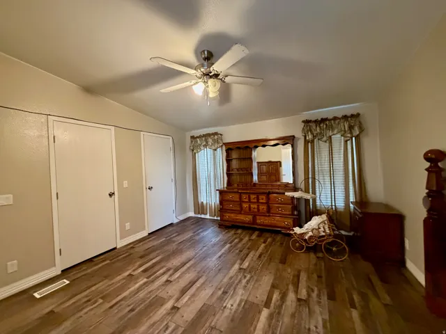 Unfurnished bedroom featuring vaulted ceiling, dark wood-type flooring, a ceiling fan, and two closets