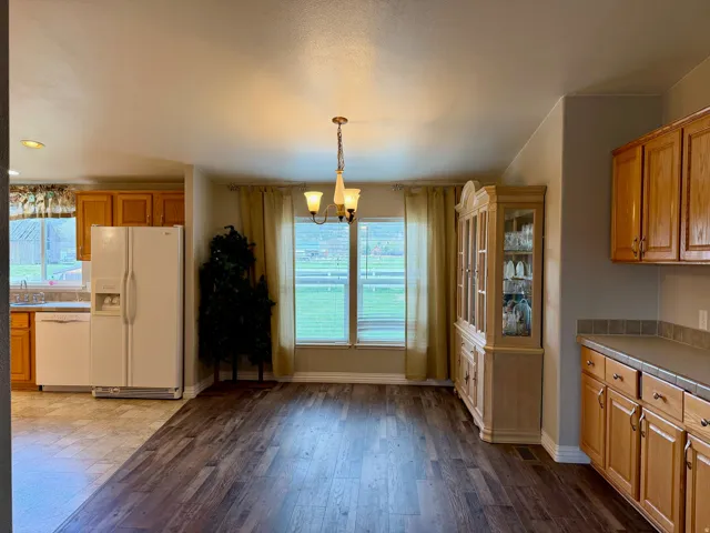 Kitchen featuring white appliances, wood finish cabinets, suspended lighting, dark wood-style flooring, and plenty of natural light