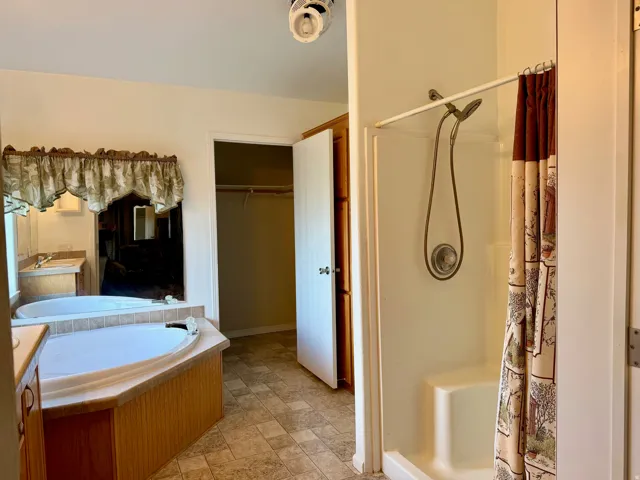 Bathroom with a shower stall, vanity, a bath, stone finish flooring, and a walk in closet