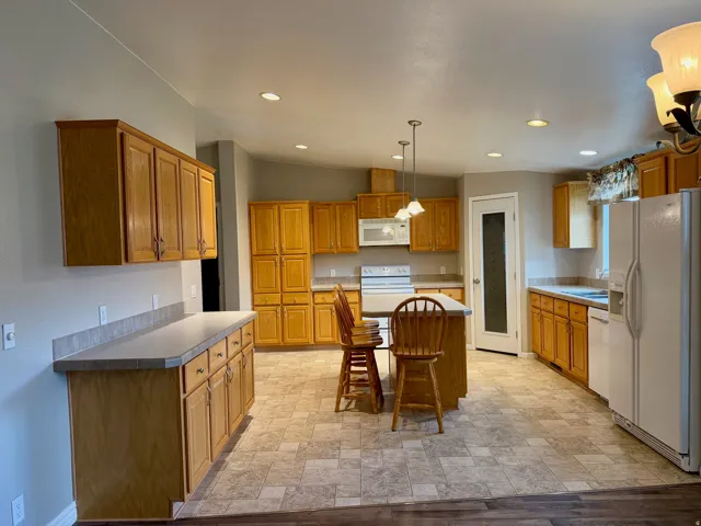Kitchen featuring white appliances, pendant lighting, stone finish floors, a kitchen island, and wood finish cabinets