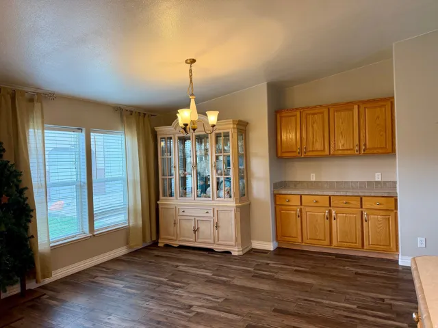 Unfurnished dining area featuring hanging lights, dark wood-style flooring, and a textured ceiling
