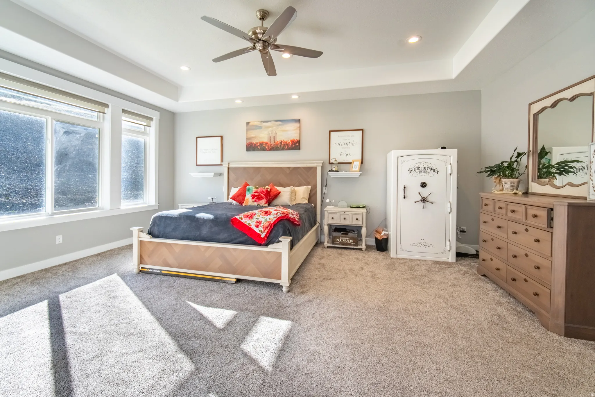 Primary bedroom featuring light colored carpet, a raised ceiling, a ceiling fan, and recessed lighting