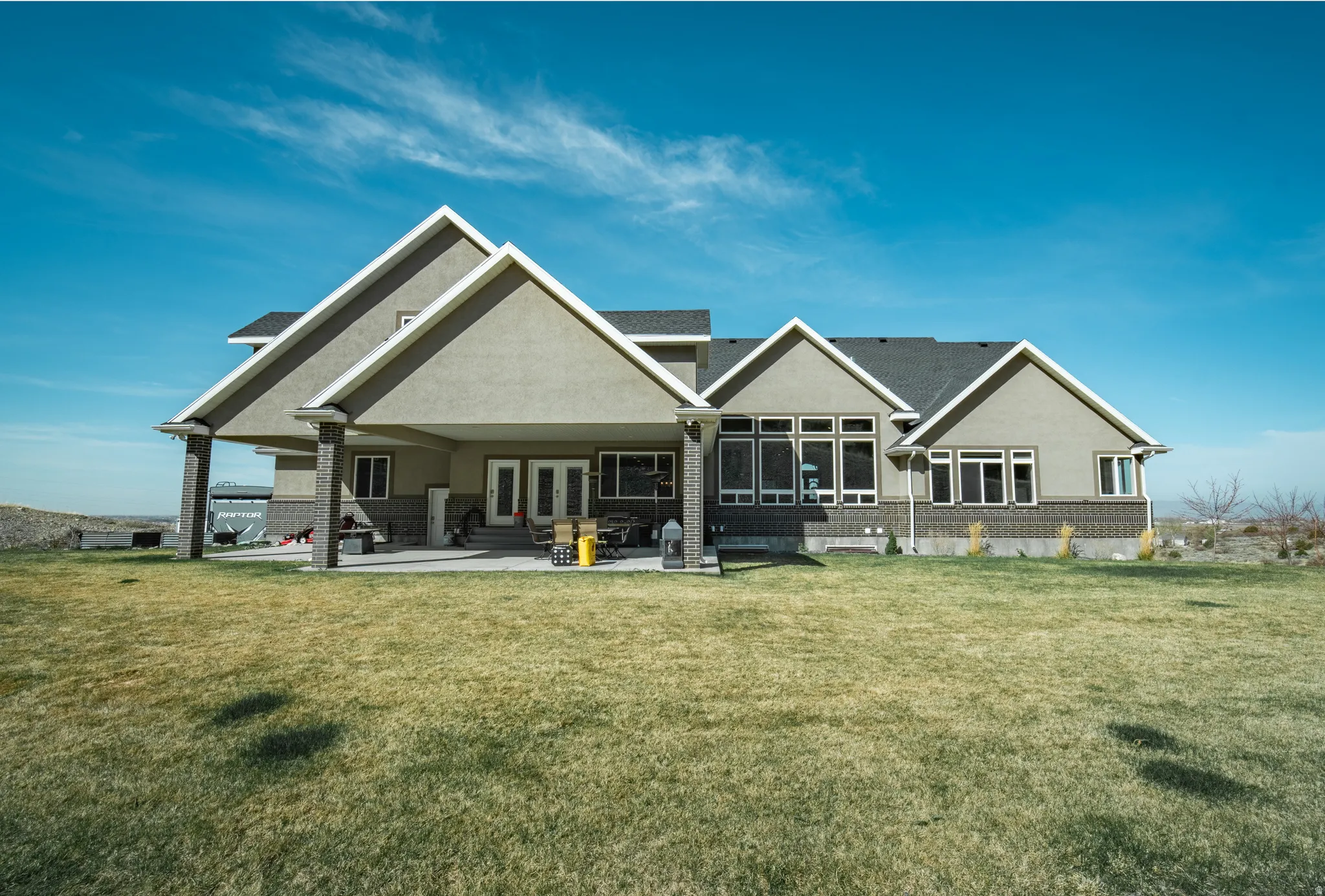 Rear view of property featuring a lawn, a patio, stucco siding, brick siding, and french doors