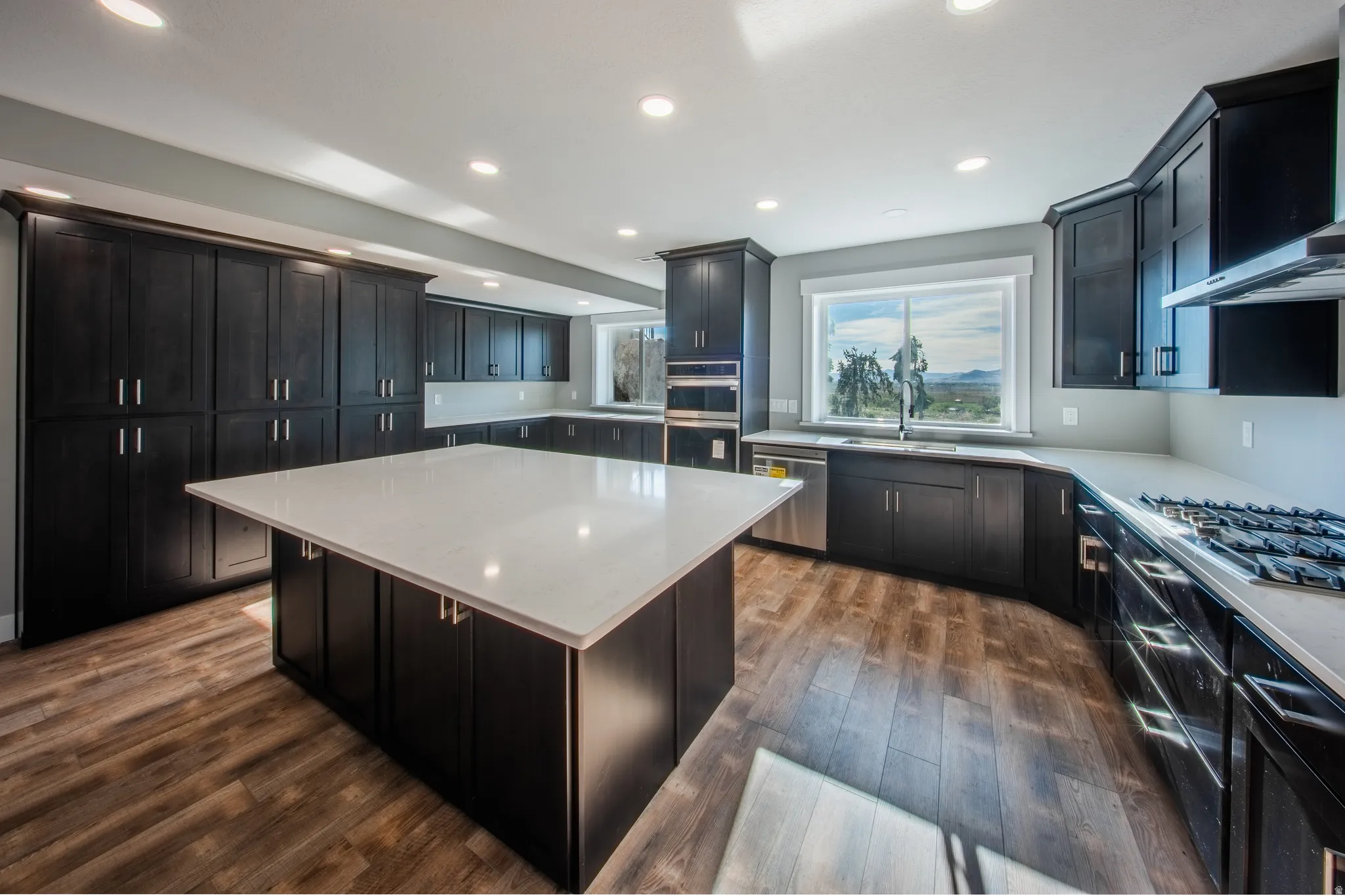 Kitchen with a center island, wood-style floors, light stone countertops, stainless steel appliances, and ventilation hood