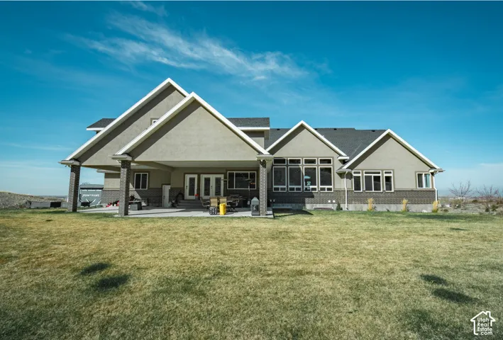 Rear view of property featuring a lawn, a patio, stucco siding, brick siding, and french doors