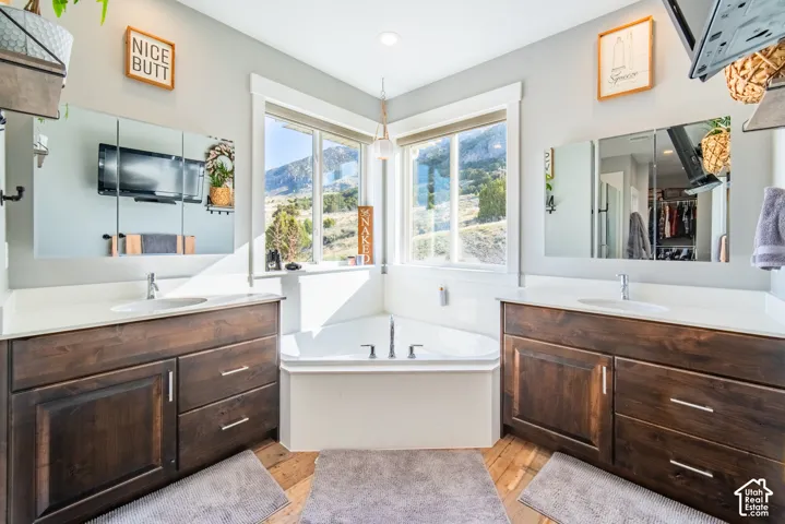 Full bath with a bath, two vanities, and light wood-style flooring