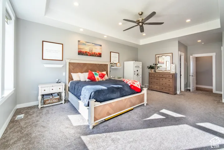 Primary bedroom with light colored carpet, ceiling fan, recessed lighting, and a tray ceiling
