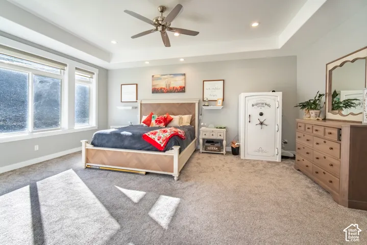 Primary bedroom featuring light colored carpet, a raised ceiling, a ceiling fan, and recessed lighting
