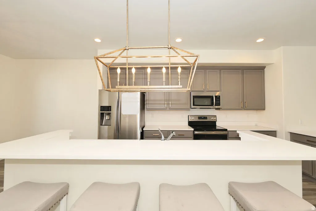 Kitchen featuring stainless steel appliances, gray cabinets, a breakfast bar area, and decorative light fixtures