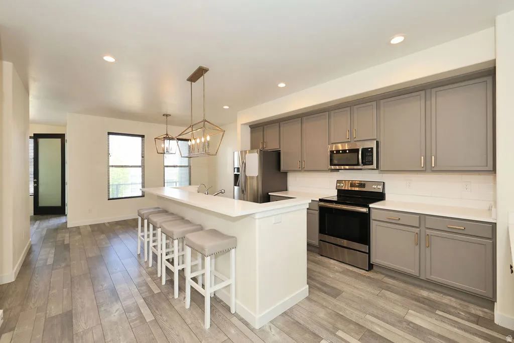 Kitchen featuring stainless steel appliances, gray cabinetry, a breakfast bar area, and light wood-style floors