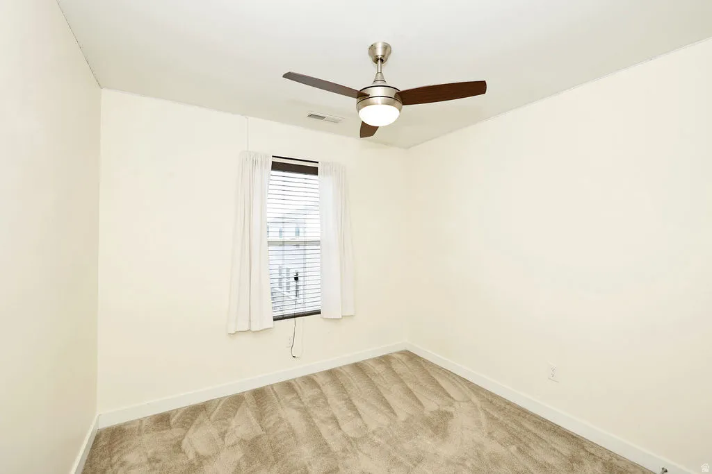 Empty room featuring light colored carpet and a ceiling fan