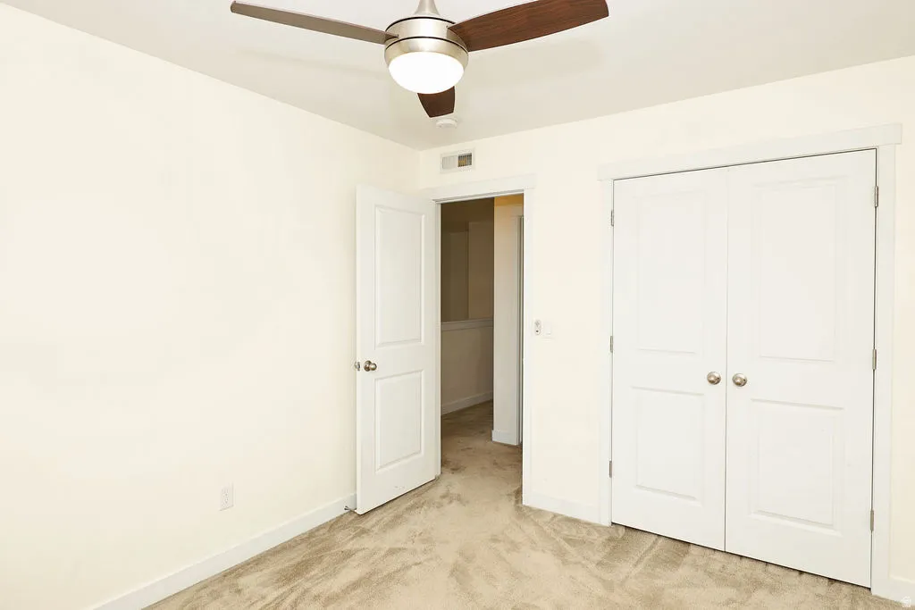 Unfurnished bedroom featuring light carpet, a ceiling fan, and a closet