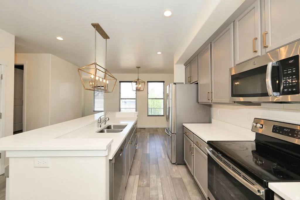Kitchen with stainless steel appliances, gray cabinetry, a center island with sink, light wood finished floors, and hanging lights
