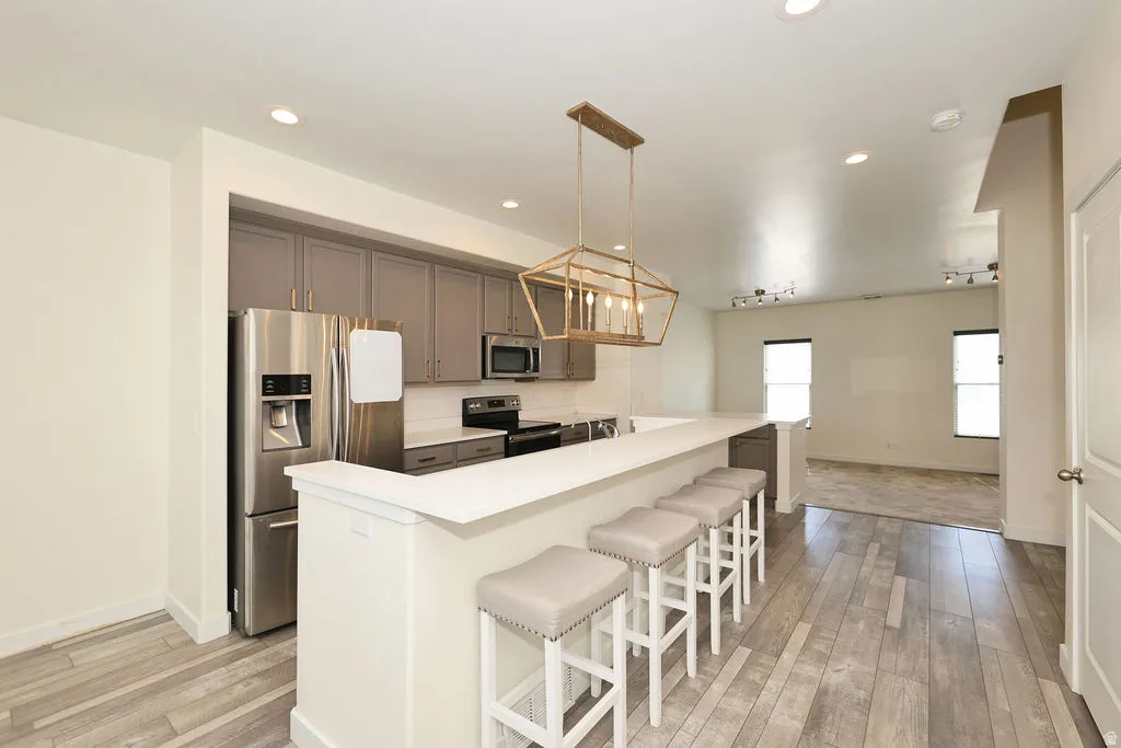 Kitchen with stainless steel appliances, a breakfast bar area, a center island, light countertops, and light wood-type flooring
