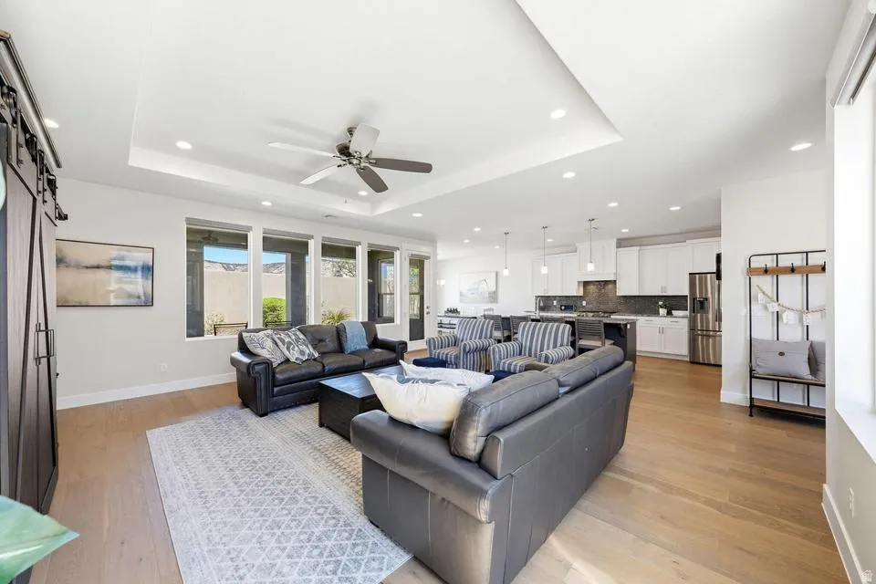 Living room with a barn door, light wood-type flooring, ceiling fan, a raised ceiling, and recessed lighting