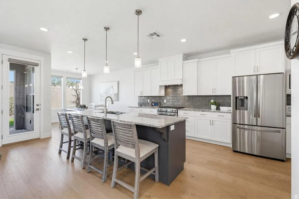 Two tone kitchen with stainless steel appliances, light stone counters, two tone cabinets, an island with sink, and light wood-style flooring