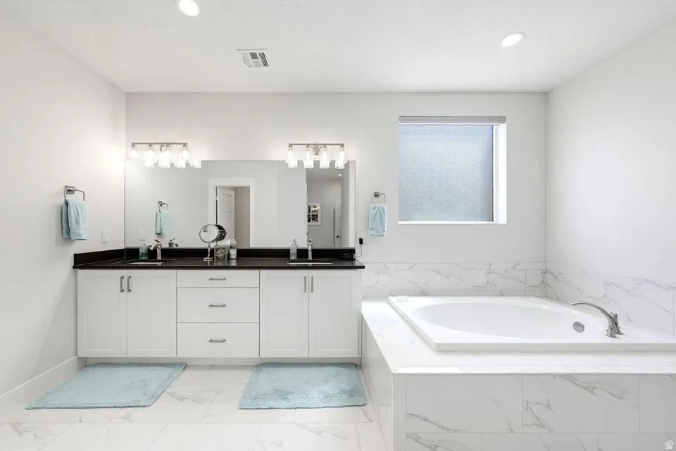 Full bath with double vanity, a bath, light marble finish flooring, and recessed lighting