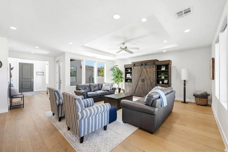 Living area with light wood-type flooring, a barn door, recessed lighting, a ceiling fan, and a raised ceiling