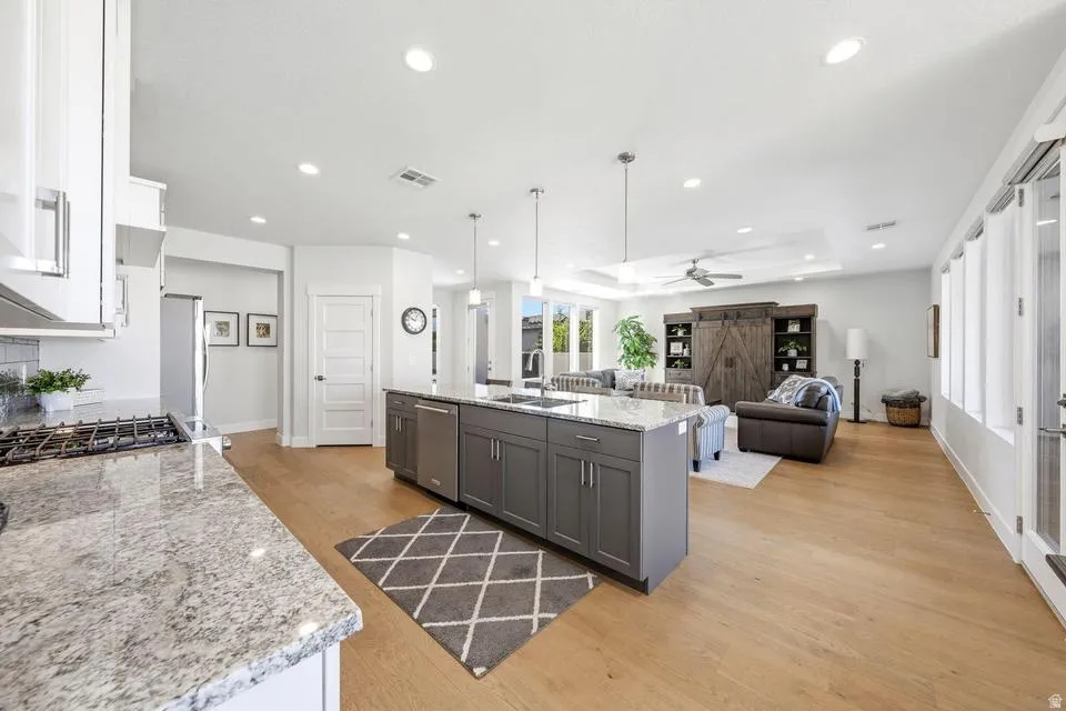 Kitchen with light stone counters, light wood finished floors, open floor plan, a kitchen island with sink, and a tray ceiling