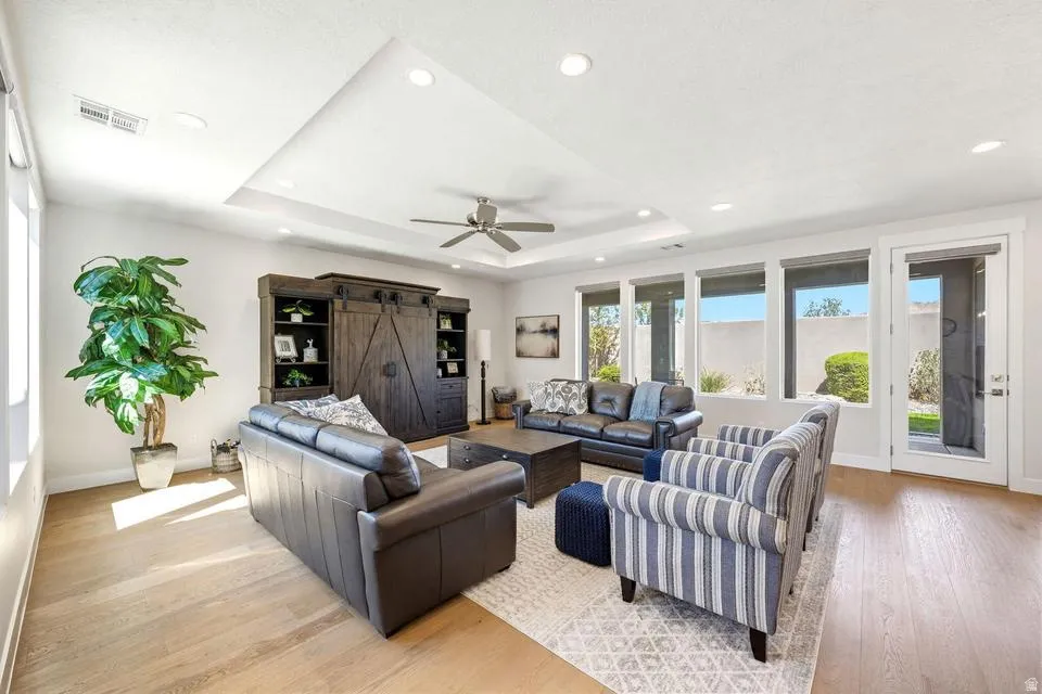Living room featuring a barn door, light wood finished floors, ceiling fan, a raised ceiling, and recessed lighting