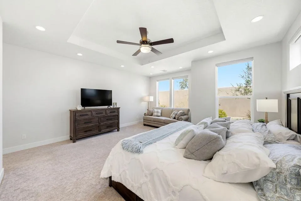 Bedroom with light colored carpet, ceiling fan, recessed lighting, and a raised ceiling